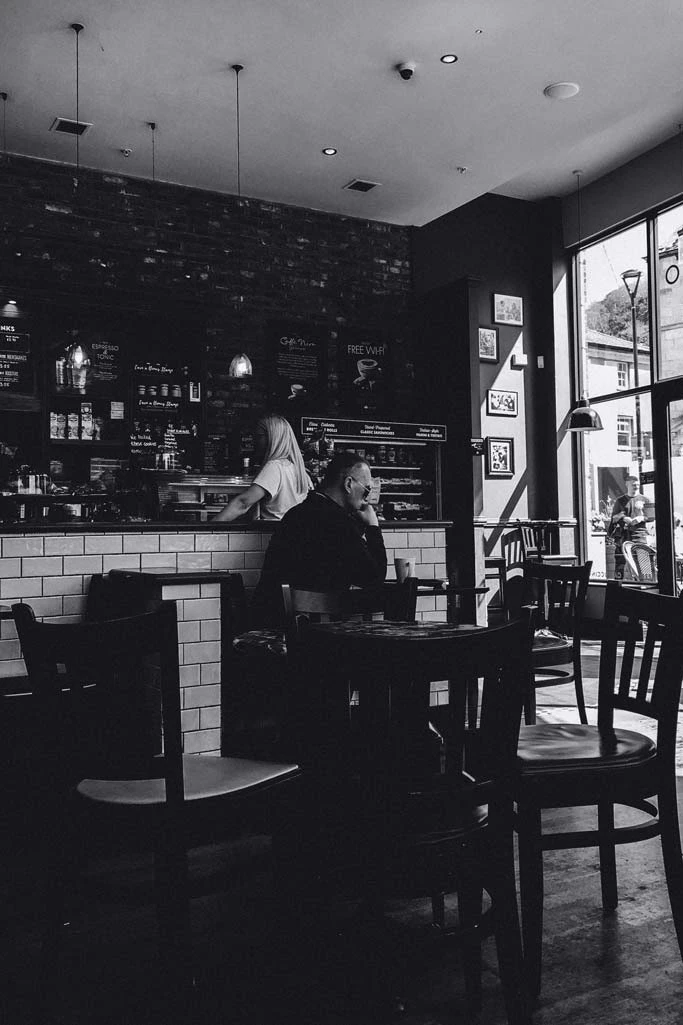 Schwarz-Weiß Foto von Bar mit Mann sitzend am Tisch und Frau an Theke.